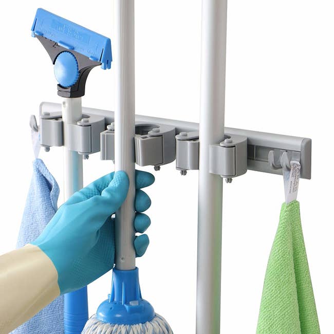 a hand reaches for a mop hanging from a mounted dr dirt mop and broom holder