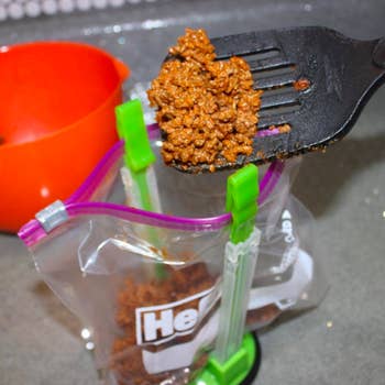 reviewer spooning meat sauce into a bag held open by the product