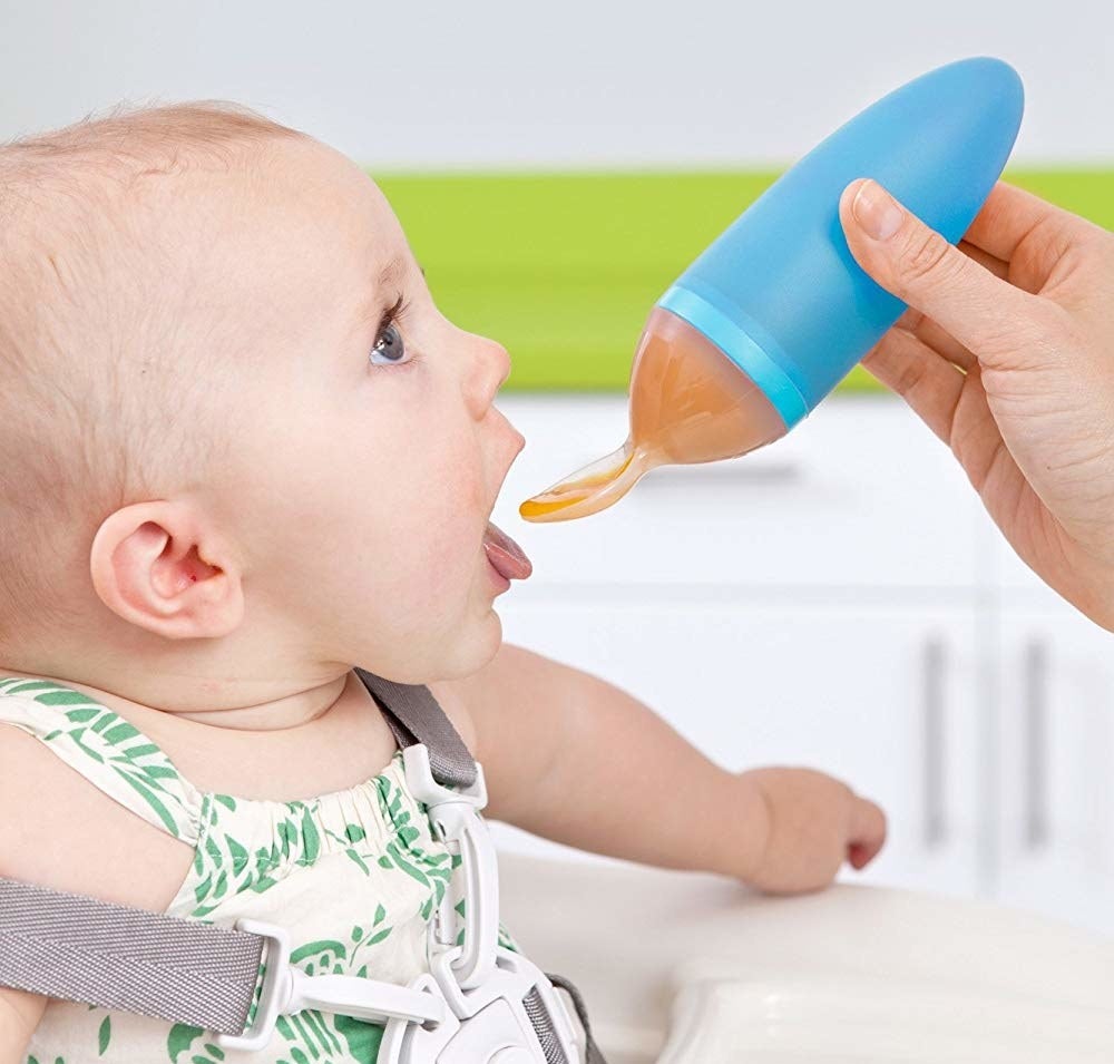 A person feeding their baby with a spoon The spoon has a large tube attached to it filled with baby food