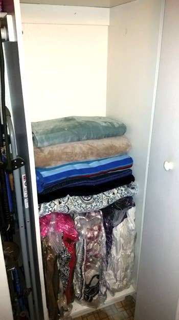 A photo shows the same closet with most of the blankets stored in vacuum-sealed bags at the bottom of it. Four blankets sit on top that aren't in the vacuum-sealed bags. There's about a foot and a half of space from its ceiling to the top blanket.