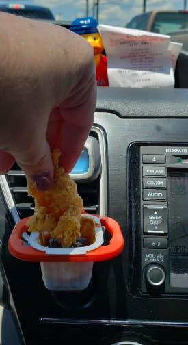 A reviewer dipping a chicken tender into a sauce cup stored in the red holder clipped to a car air vent