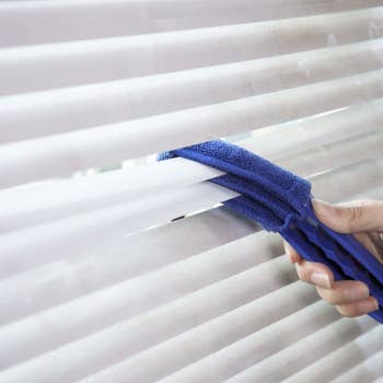 hand cleaning the top and bottom of two blinds at once using the blue brush