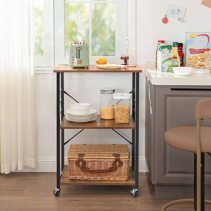 The rolling cart with dark wood shelves and black frame with wheels in a kitchen