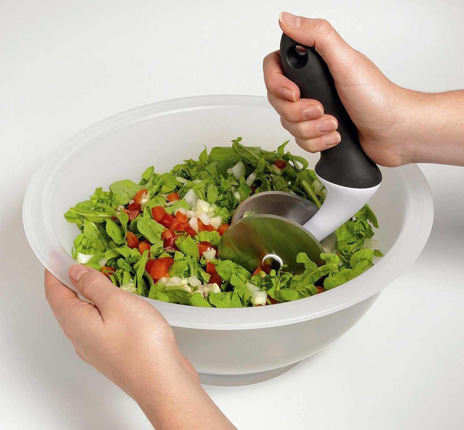 A person rolls the chopping tool in the bowl to prep salad