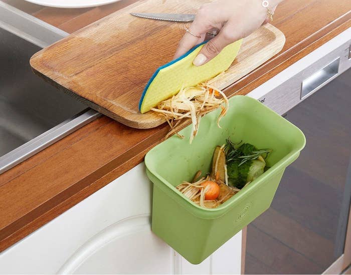 A hand using a sponge to brush food scraps into the bin