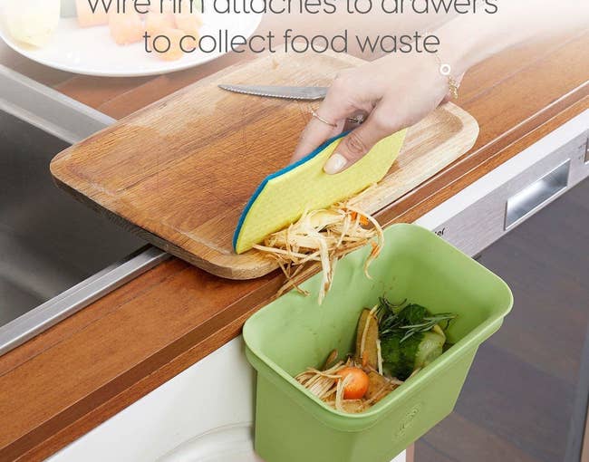 A hand using a sponge to brush food scraps into the bin