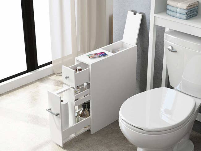 The cabinet with its drawers opened showing the variety of items it can store next to the toilet