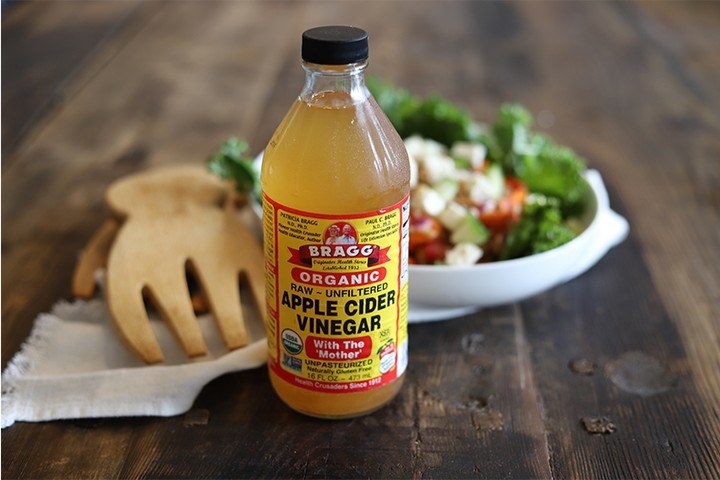 A bottle of apple cider vinegar with a large salad in the background