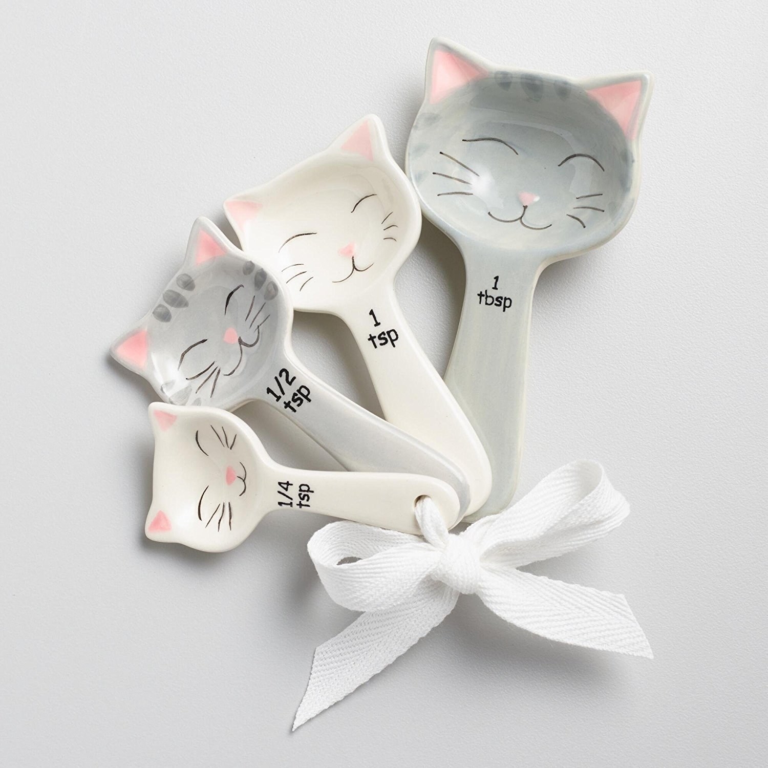 A set of 1/4 tsp, 1/2 tsp, 1 tsp, and 1 tbsp measuring spoons with happy cat faces painted on them tied with a white ribbon