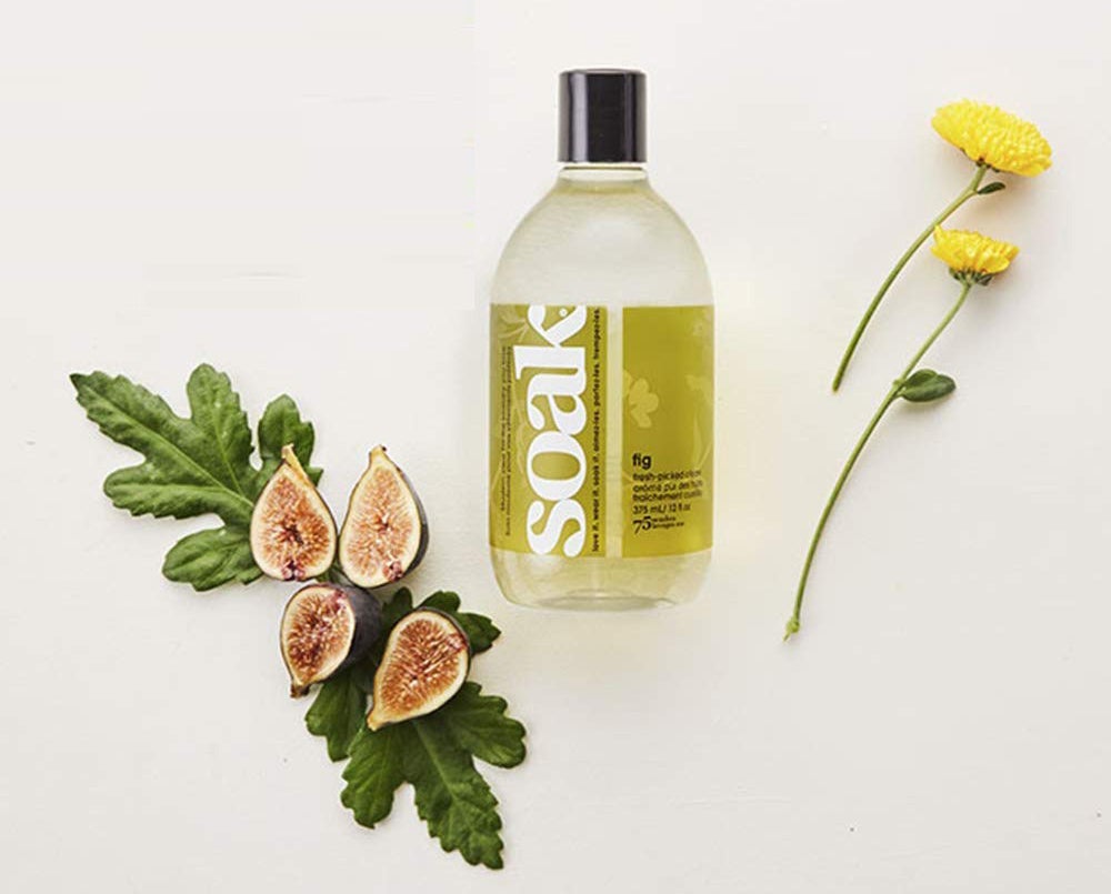 A bottle a laundry soap with flowers and sliced figs beside it