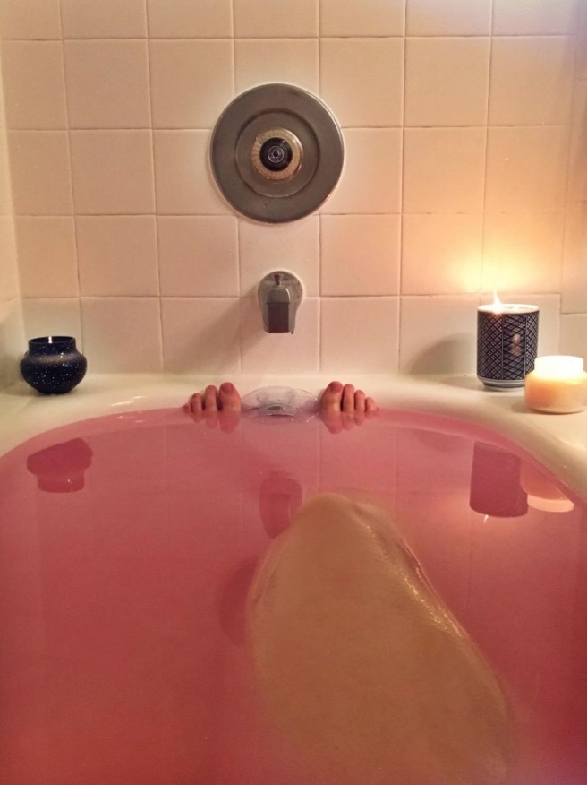 The drain cover in a bath with pink water surrounded by candles
