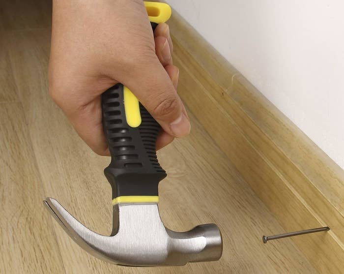 A person hammering a nail into a wall using a claw hammer