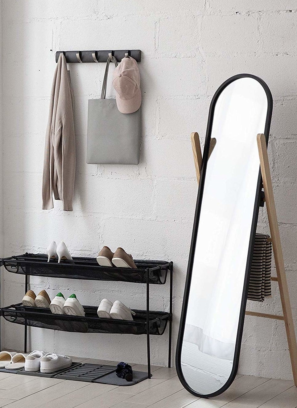 The ladder shelf with a blanket hanging from its back standing next to a shoe shelf and a wall-mounted rack