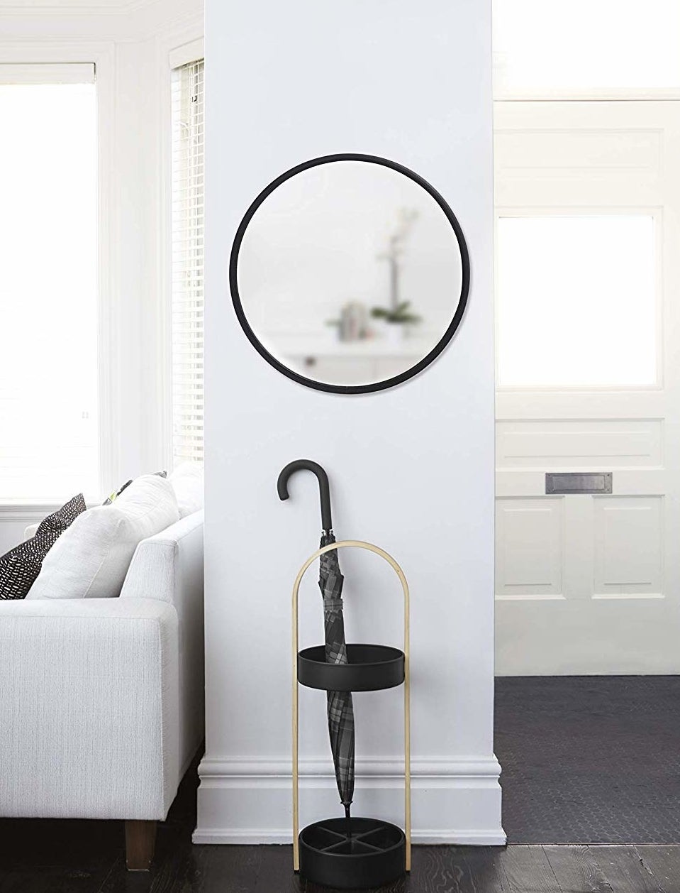 The round mirror is hung on a narrow wall above an umbrella stand