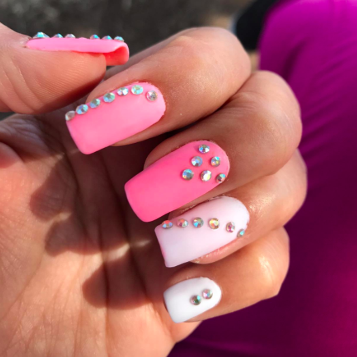 person showing their pink nails with nails jewels on them after using the top coat