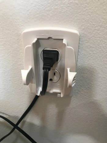 A reviewer's photo of the open outlet cover with a cord plugged in