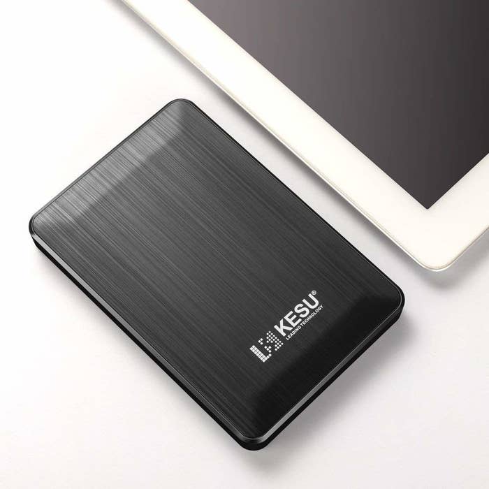 A small rectangular external hard drive lying next to a tablet