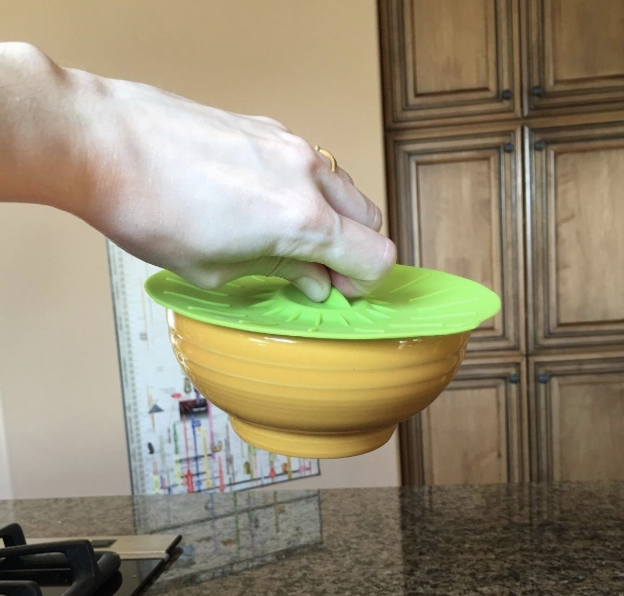reviewer&#x27;s hand holding up a bowl by the microwave cover top that&#x27;s on top of it