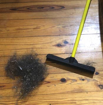 A photo of the same yellow and black squeegee broom on a hardwood floor with a big clump of hair that's presumably been corralled by the broom.