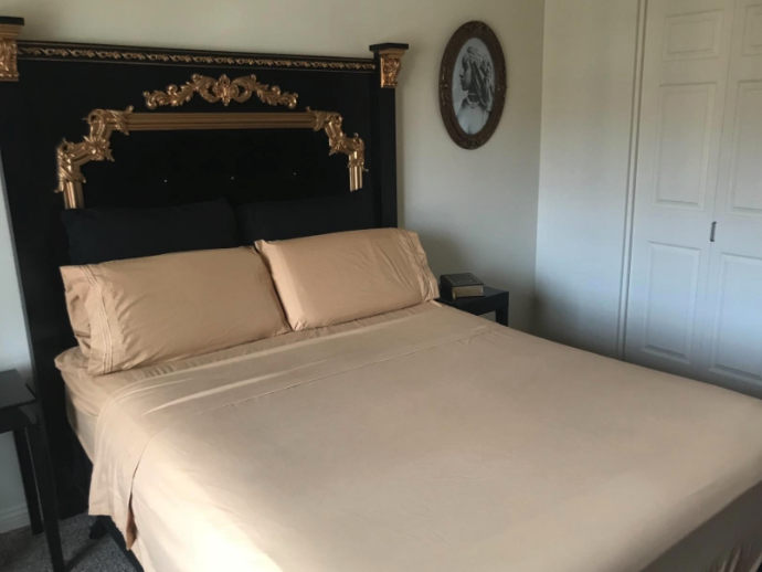 The photo shows a bed with a black headboard that features gold team. On it, you see a taupe fitted and top sheet on the bed and two pillows with matching taupe pillowcases. The bed doesn&#x27;t have a blanket on it. Just the sheet and pillow set.