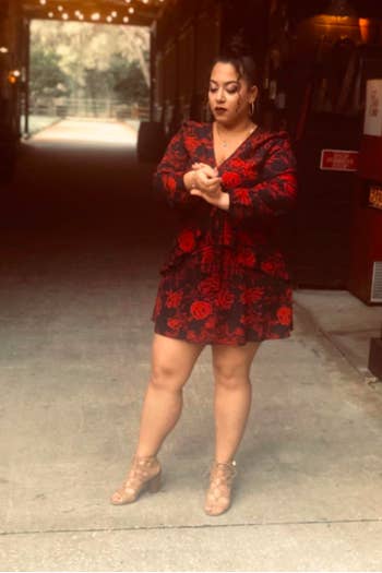 A reviewer wearing the long-sleeve black dress printed with red roses