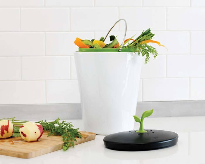 small white bin with handle, food scraps inside and a black lid next to it
