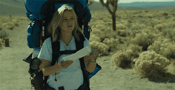 A gif from the movie Wild of Reese Witherspoon holding a map in the desert with a large backpacking pack on. 