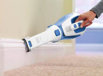 The handheld vacuum being used to clean baseboards