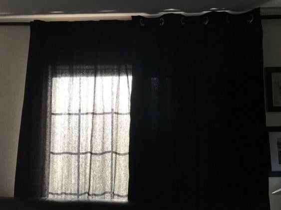 Window with regular black curtains on one side with light shining through. The blackout curtain is on the other side and has no light shining through at all.
