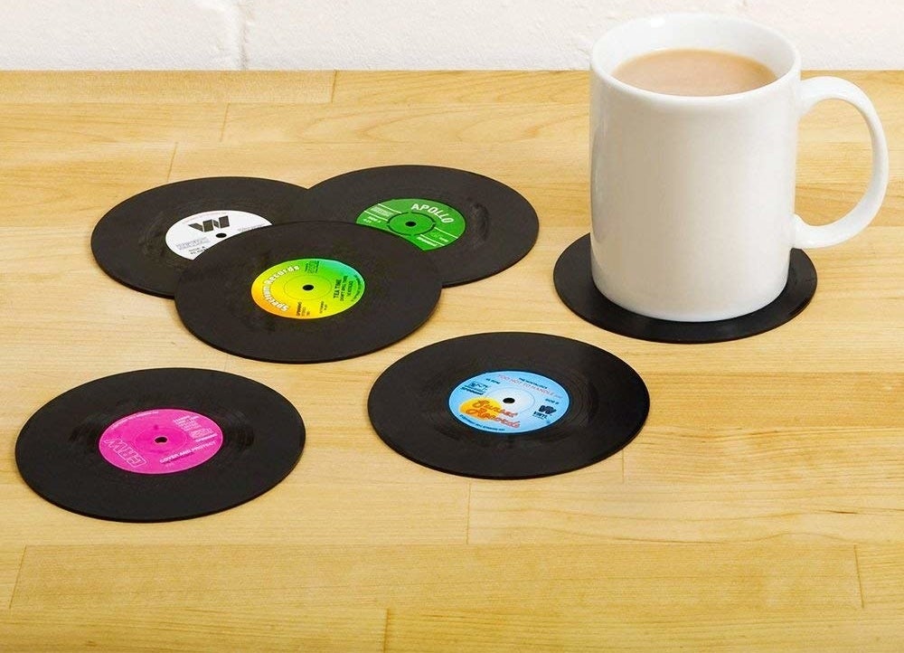 A set of six plastic coasters that look like vinyls One coaster has a coffee mug resting on it