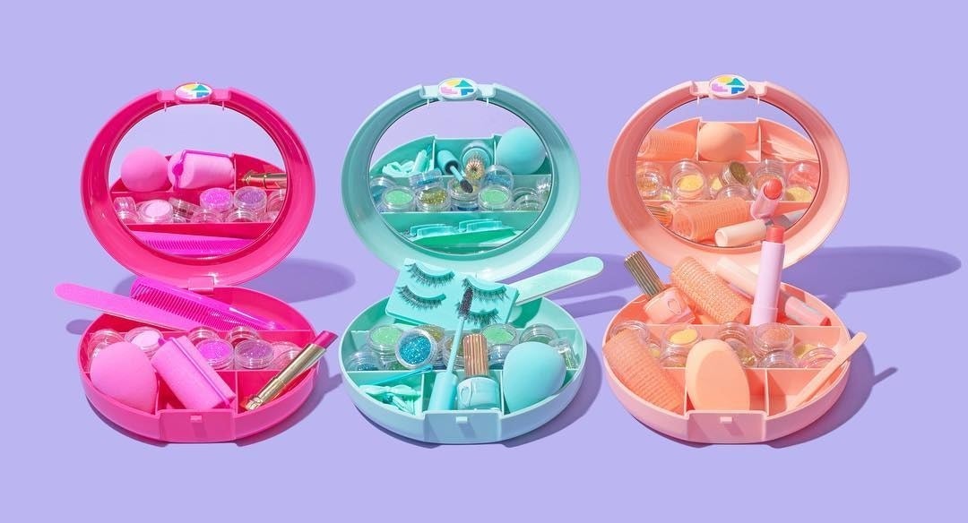 Three sets of small makeup cases in a line They are all open with a mirror the inside of the lid and little compartments on the bottom that are filled with various beauty products 