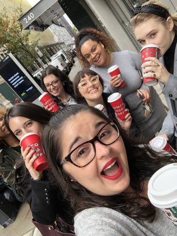 a buzzfeed editor wearing the red lipstick while posing with a group of people with starbucks cups