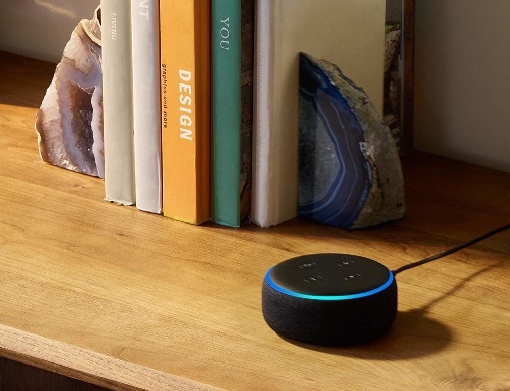 An Echo Dot beside a stack of books on a shelf