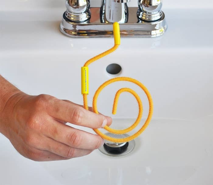 A person holding a coiled mini drain snake in front of a sink