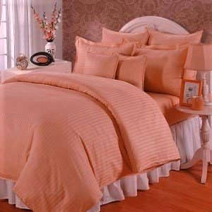 A peach duvet cover on a bed next to a table with a lamp on it