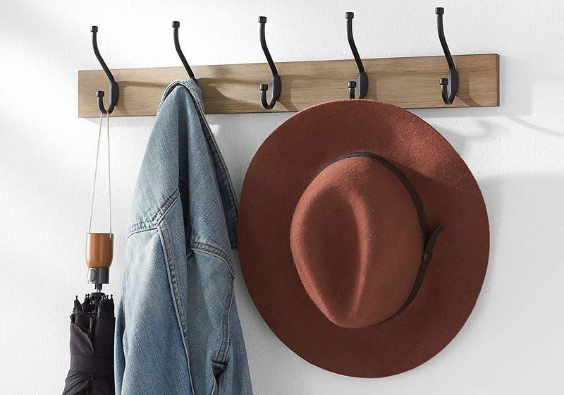 wall mounted coat rack holding a coat, a hat, and an umbrella