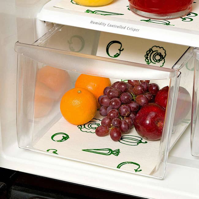 open fridge with drawer inside that has the liner underneath oranges, grapes, and apples