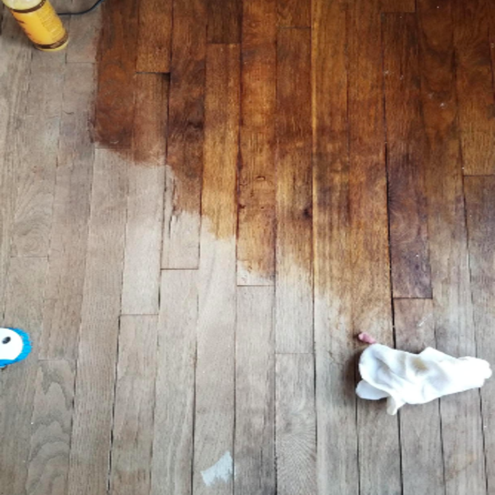 reviewer pic of a dry old wood floor that looks gray with half of it looking refreshed thanks to the wood polish