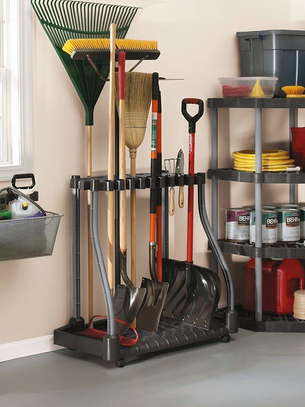 A tool stand holding a rake, two shovels, a garden rake, two brooms, and a snow shovel