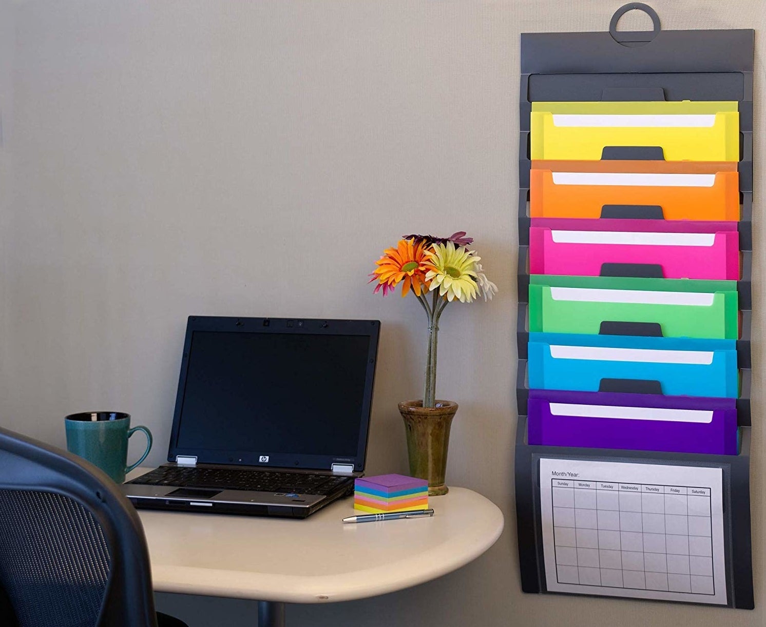 A vertical file folder hanging from the wall next to a table with a laptop
