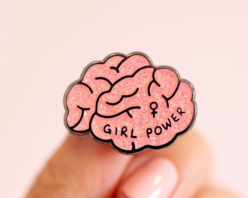 A pink glitter pin shaped like a brain with the text "girl power" and the female symbol