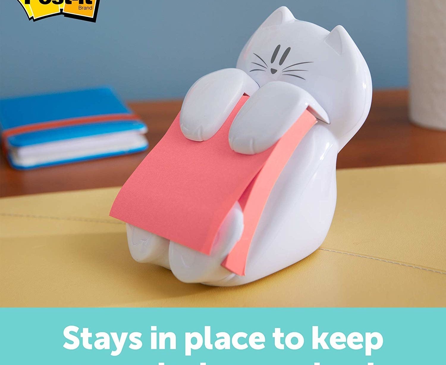 The cat-shaped sticky note dispenser sitting on a table holding a pad of pink stinky notes