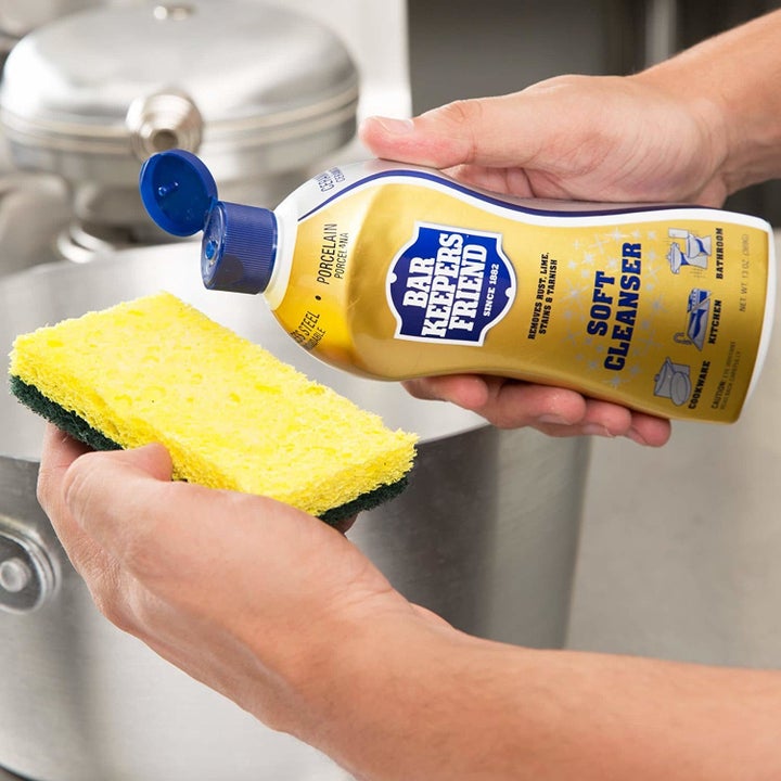 A person drops a bit of the product onto a cleaning sponge while stainless steel accessories are seen in the background
