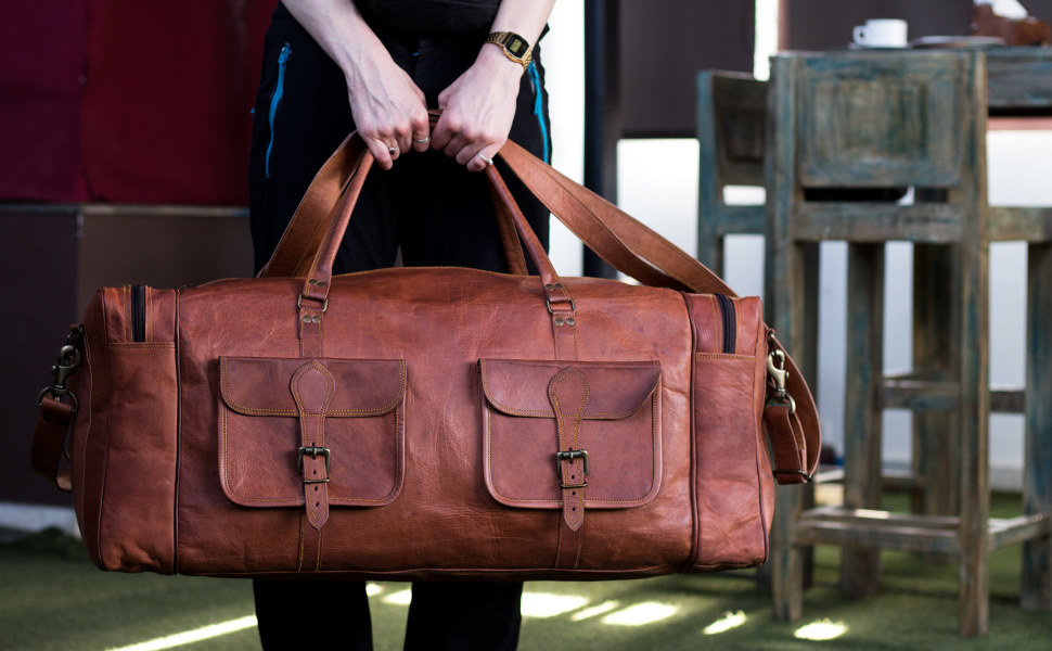 model holding a large leather duffel bag with two front pockets