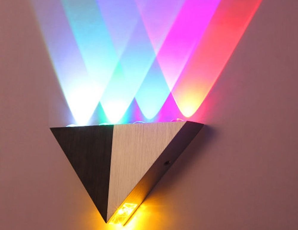 A black and white scone installed on a wall with different coloured lights being projected from it