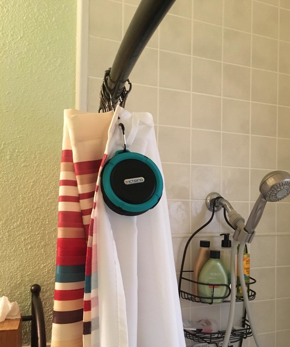 A round shower speaker attached to a shower curtain rod 