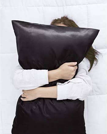 Model hugging a black satin pillow 