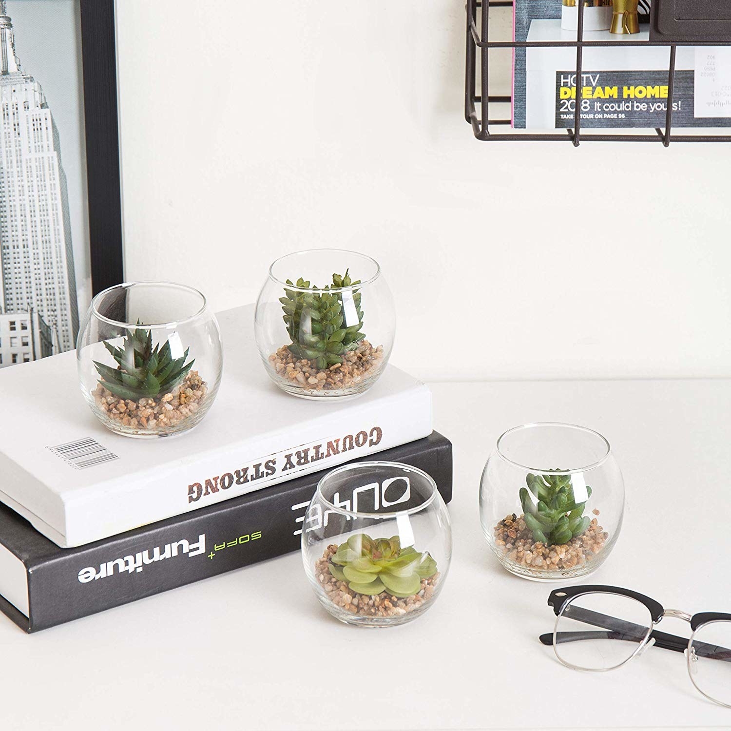 four succulents styled next to books and glasses on a white table 