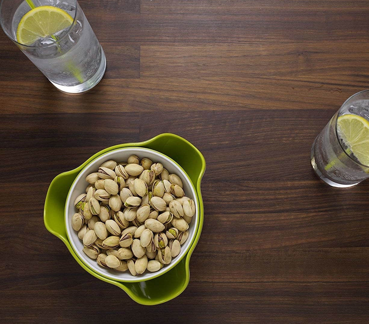 A flatlay of the bowl filled with pistachios next to some frosty drinks