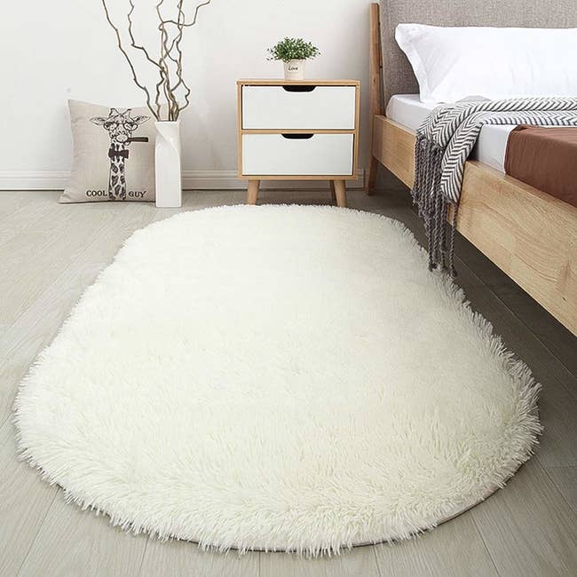 A white oval-shaped shaggy rug at the side of a bed 